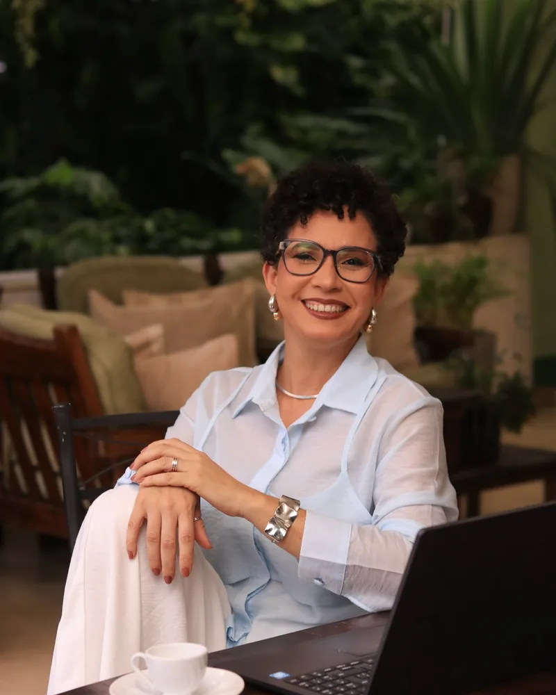 Nai Moraes sorrindo em frente ao notebook, com um café